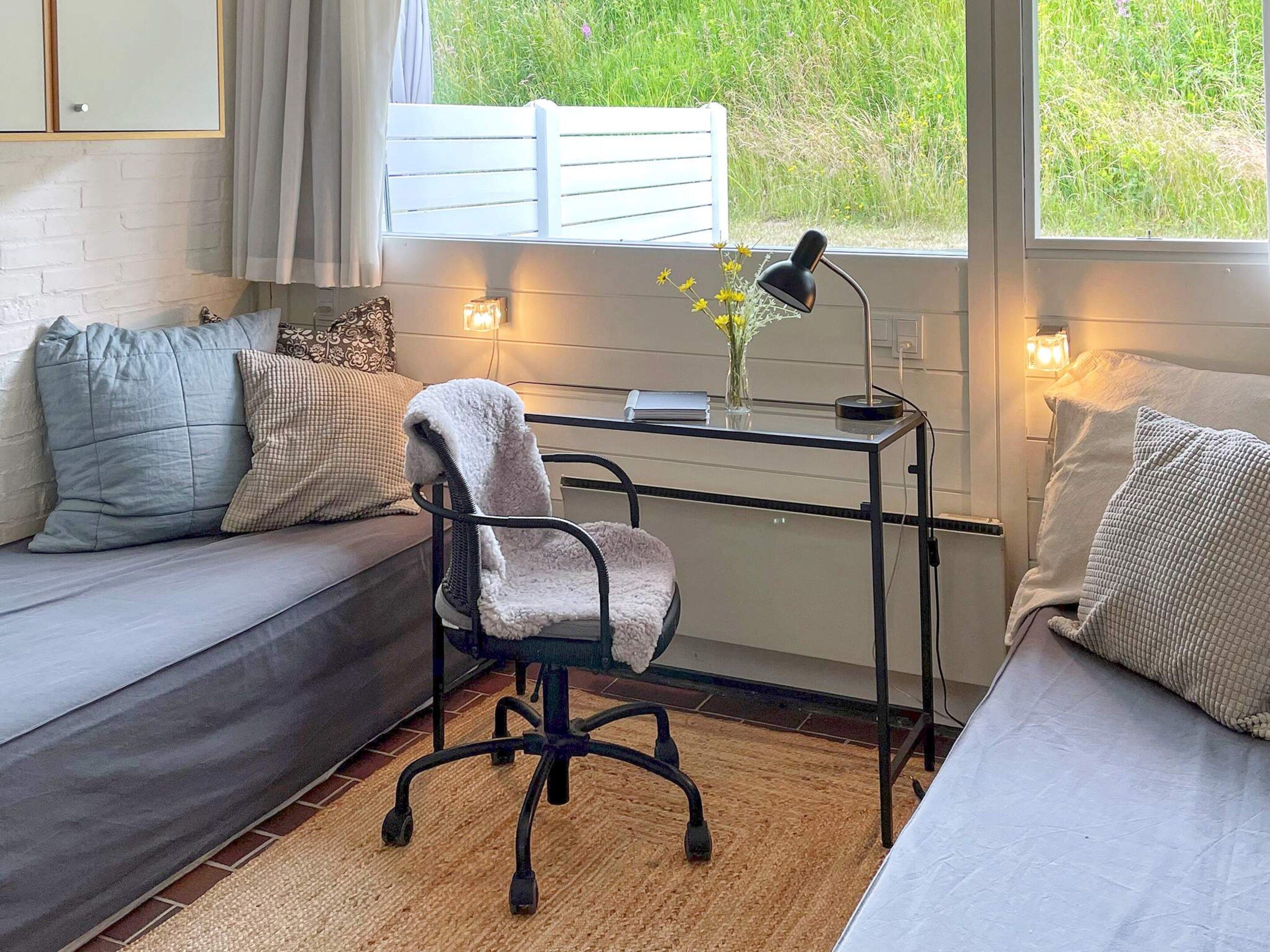 Une pièce confortable avec un canapé, un bureau et une chaise. Une fenêtre offre une vue sur la verdure environnante.