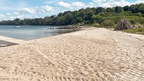 Ein sandiger Strand mit freiem Blick auf das Wasser, einer Anlegestelle und einem Haufen Äste.