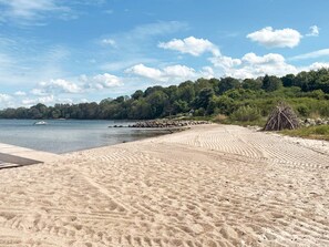 A sandy beach with a clear sky, a body of water, and a forested area in the background. - 5 Star Holiday Home in Aabenraa (Aabenraa)