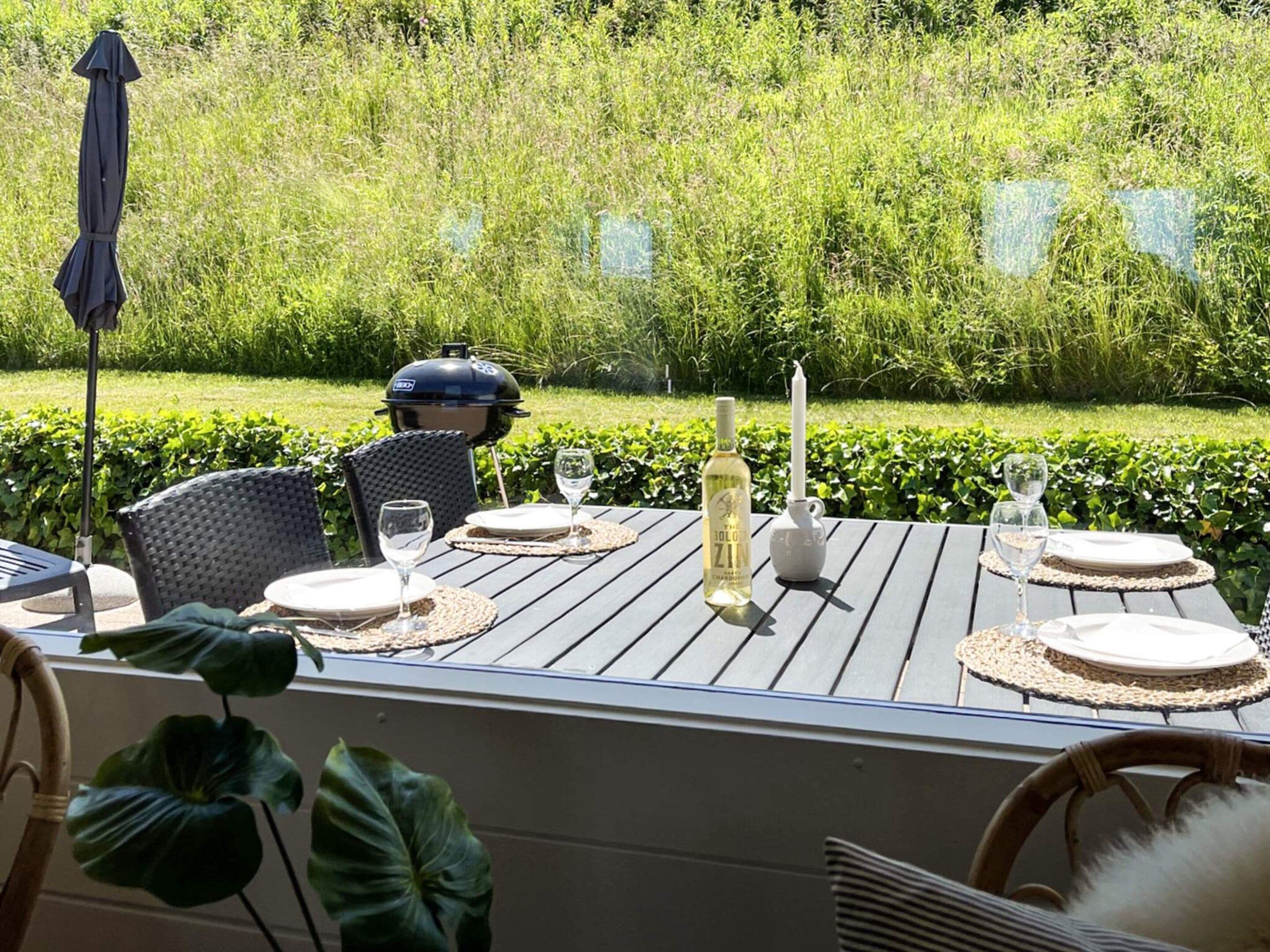 An outdoor dining area with a table set for four, surrounded by greenery.