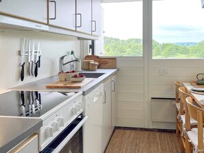 A modern kitchen with white cabinets, a stove, and a window offering a view of greenery. - 5 Star Holiday Home in Aabenraa (Aabenraa)