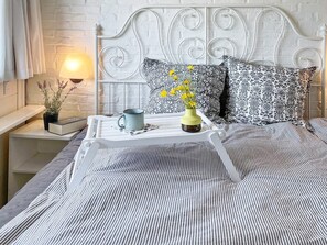 A bed with a white metal headboard, a bedside table with a lamp, a tray with a mug, a book, and a vase with flowers. - 5 Star Holiday Home in Aabenraa (Aabenraa)