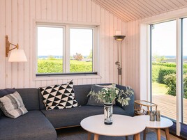 Una habitación con sofá, mesa, un florero con flores y vistas al exterior con vegetación.