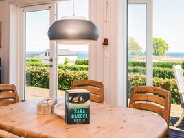 Un comedor con una mesa, sillas, un libro y vista al mar a través de amplios ventanales.