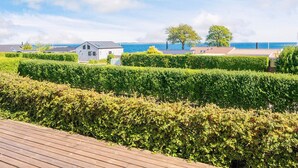 A coastal property with a wooden deck, neatly trimmed hedges, and a small white building with a sloped roof. - Alluring Holiday Home in Haderslev near Sea (Hejls)