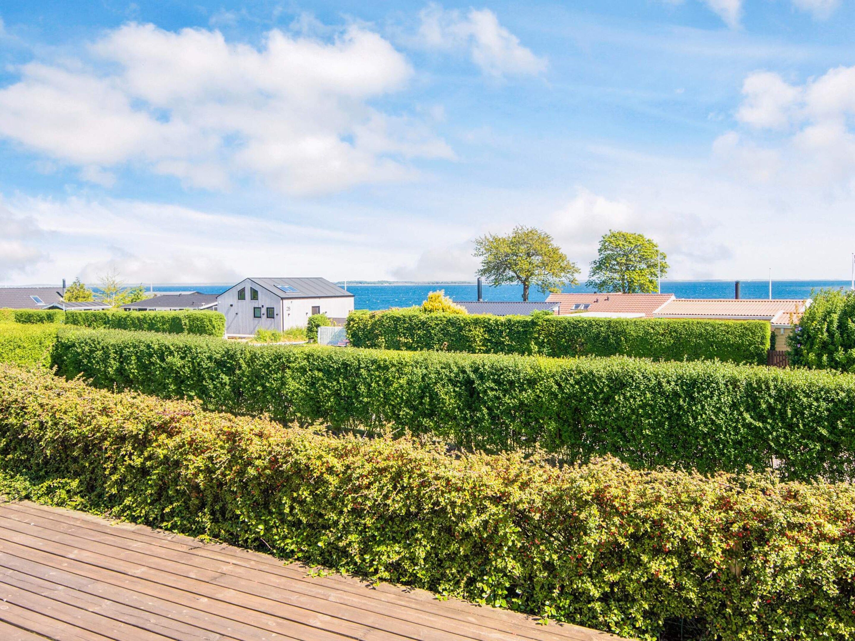 A coastal property with a wooden deck, neatly trimmed hedges, and a small white building with a sloped roof.