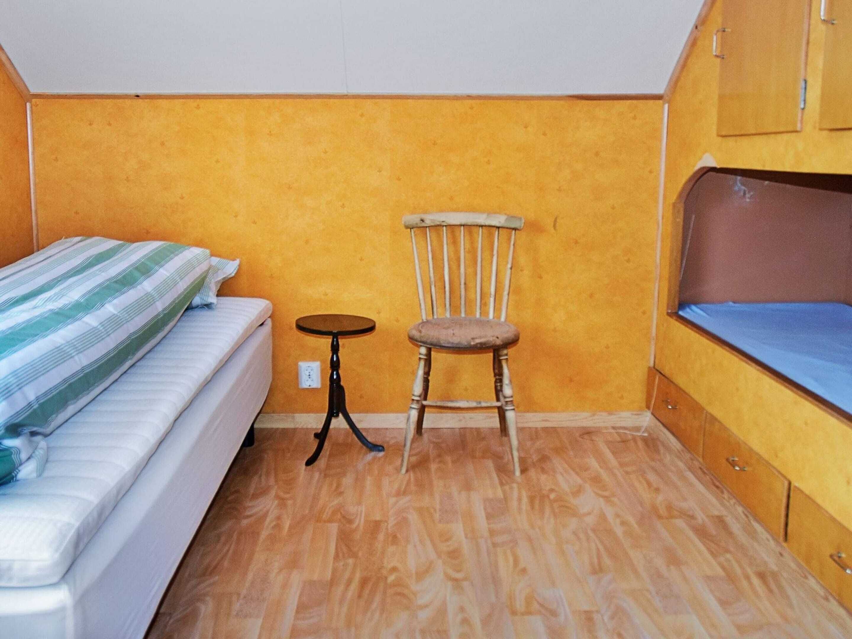 A small room with a bed, a chair, a small table, and wooden cabinets.