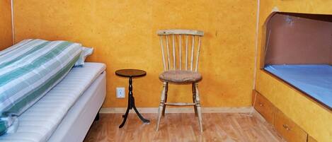 A small room with a bed, a chair, a small table, and wooden cabinets.