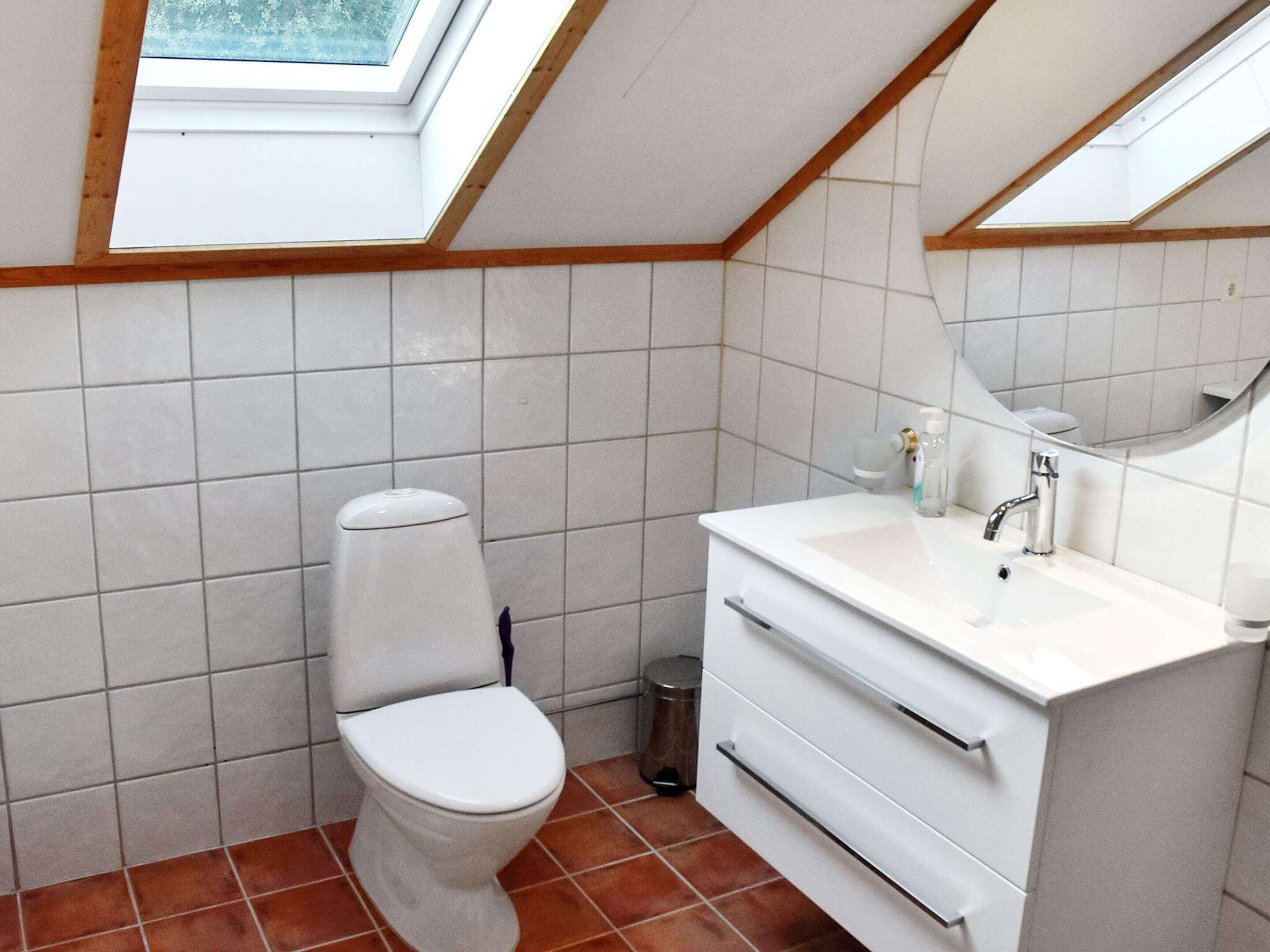 A bathroom with a toilet, sink, and mirror, featuring tiled walls and a sloped ceiling with skylights.