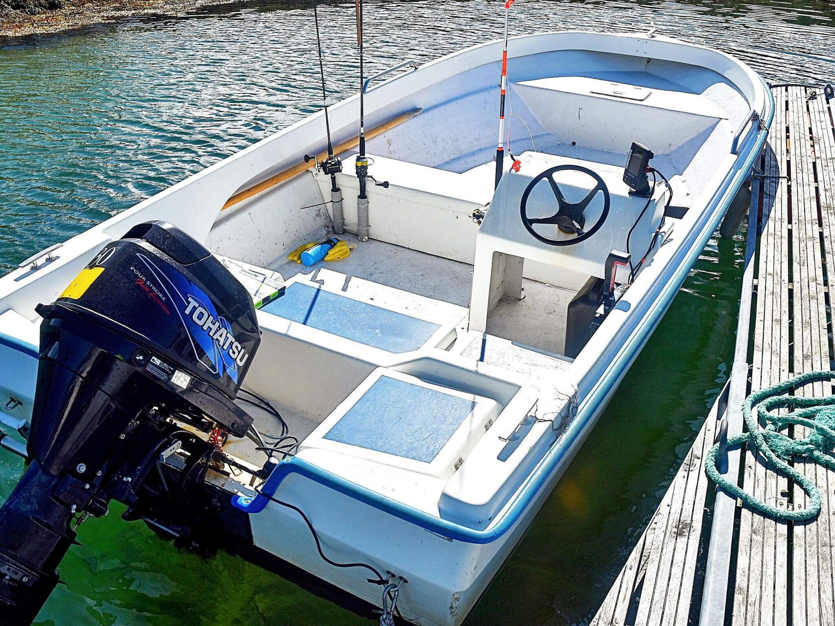A small motorboat docked at a wooden pier with a visible outboard motor, a steering wheel, and a fishing rod.