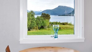 A room with a window overlooking a lake and mountains, a wooden table, and a chair.