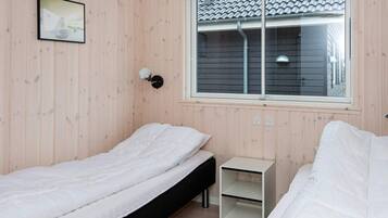 A room with two single beds, a small bedside table, a wall-mounted lamp, and a window with a view of a building.