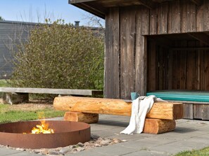 A rustic outdoor seating area with a fire pit, wooden benches, and a wooden structure. - 5 Star Holiday Home in Norre Nebel (Norre Nebel)
