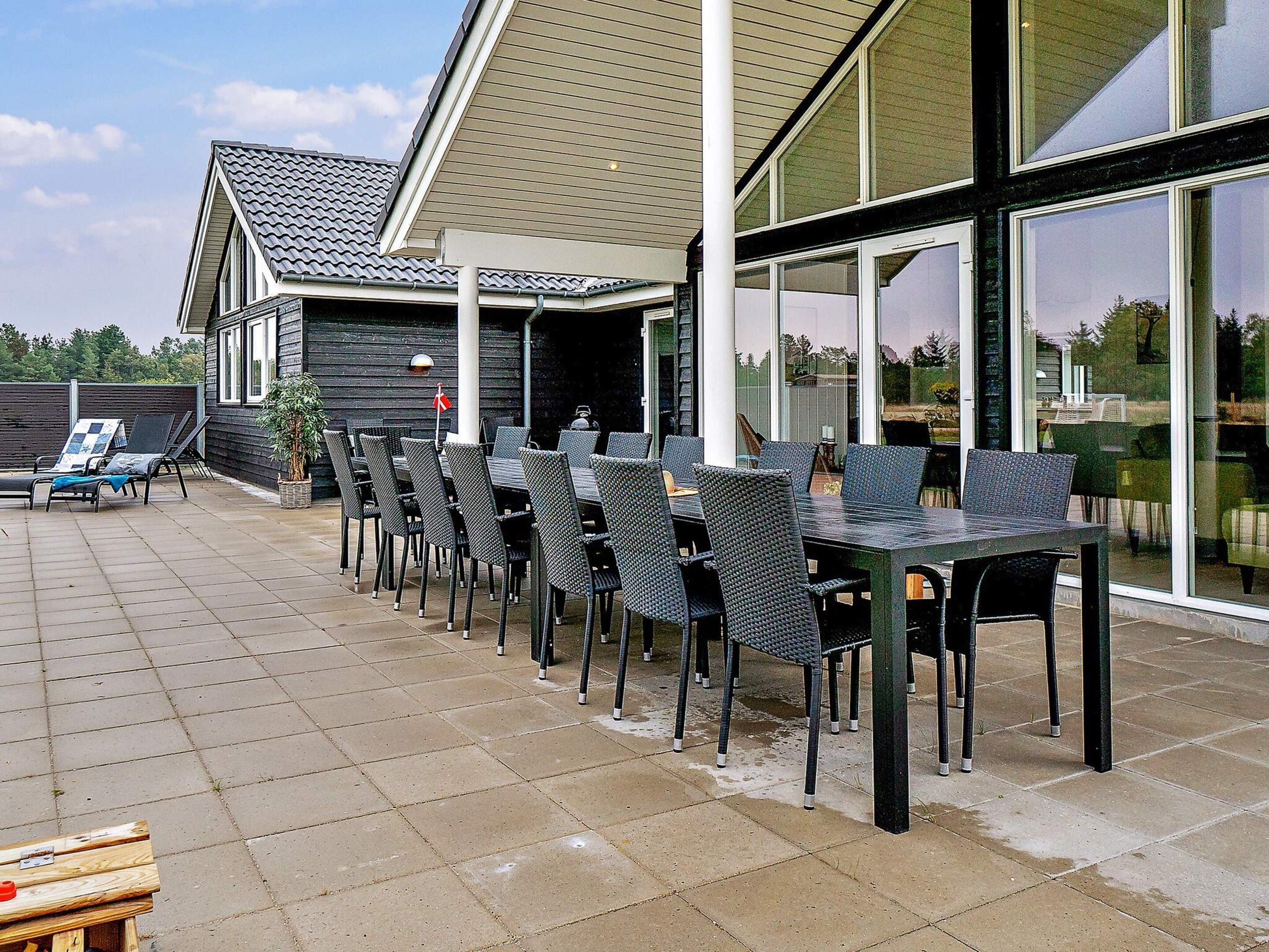 An outdoor patio with multiple tables and chairs, a wooden deck, and a building with large windows.
