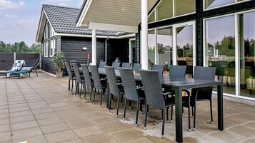 An outdoor patio with multiple tables and chairs, a wooden deck, and a building with large windows.