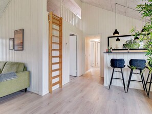 Quarto com escada de madeira, sofá verde, área de bar com banquetas e luminária pendente.
