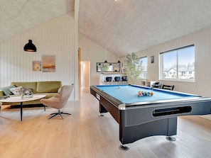 A pool table with balls, a green sofa, and a dining table with chairs.