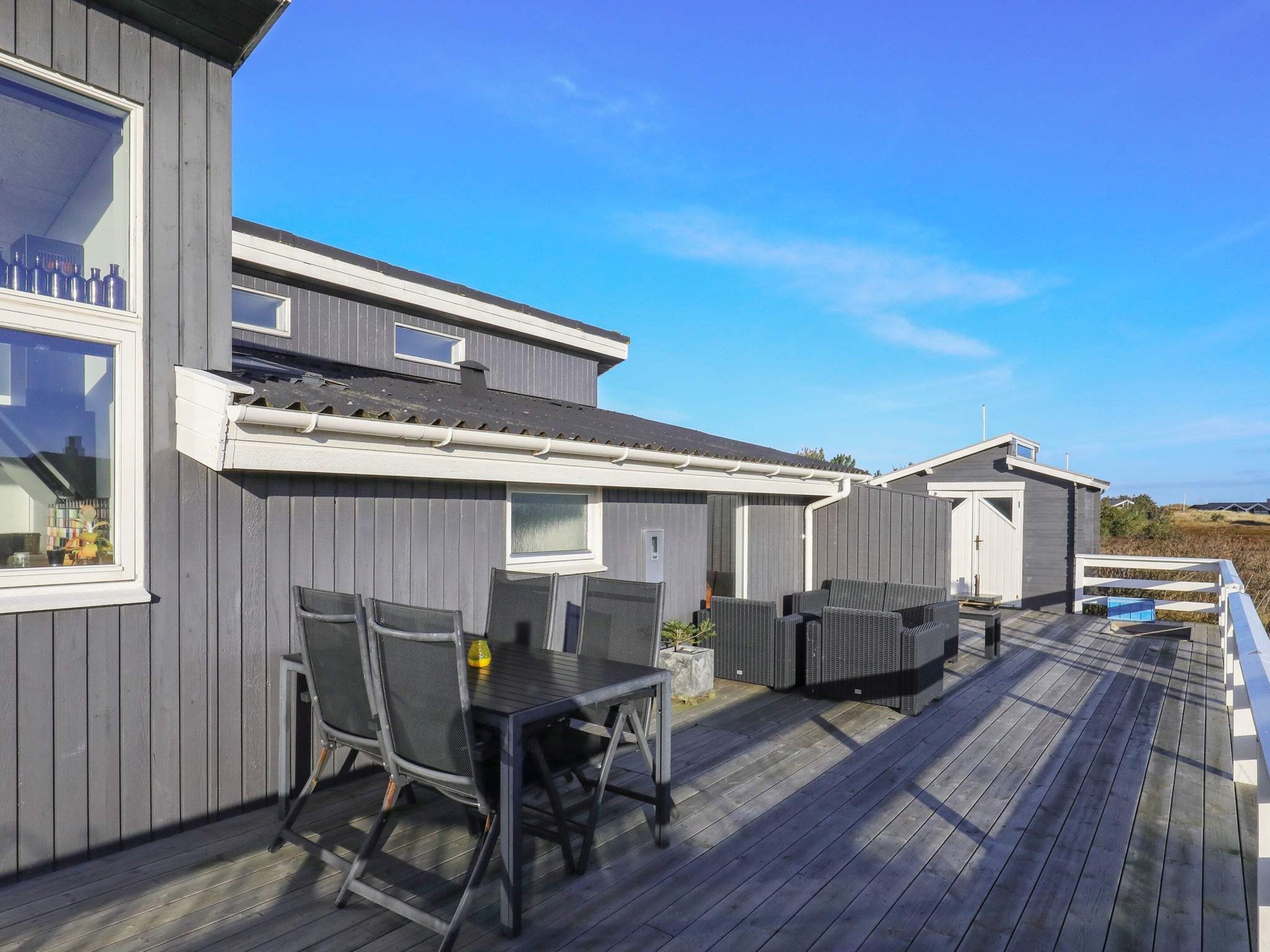 A wooden deck with outdoor furniture, a pool, and a building with multiple windows and doors.