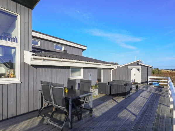 A wooden deck with outdoor furniture, a pool, and a building with multiple windows and doors.
