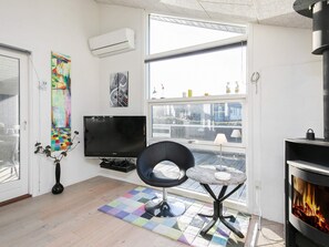 A modern living room with a flat-screen TV, a black chair, a small round table, a colorful rug, and a fireplace. - 5 Star Holiday Home in Ringkobing (Ringkobing)