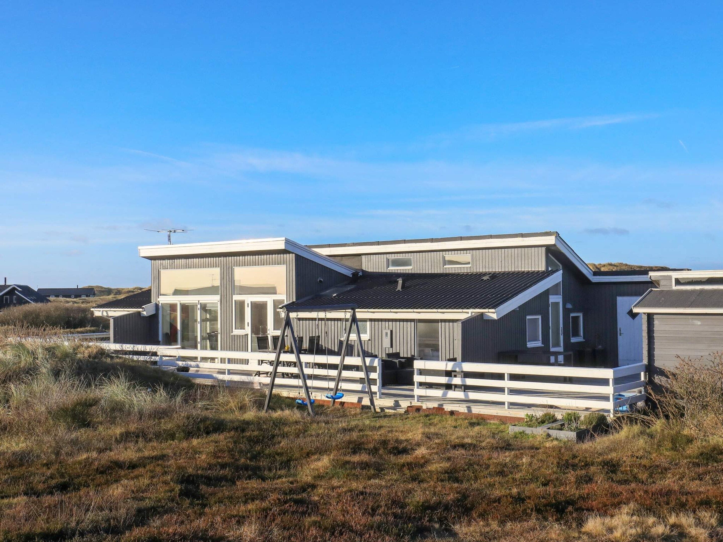Ein modernes, zweistöckiges Haus mit flachem Dach und großen Fenstern, eingebettet in eine natürliche Landschaft.