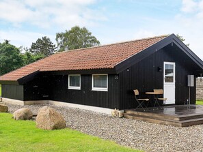 A black building with a sloped roof, a porch with chairs, and a gravel driveway. - 5 Person Holiday Home in Otterup (Otterup)