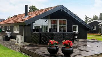 A black cabin with a sloped roof, a deck with two large planters, and a chimney.