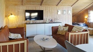A cozy room with a wooden ceiling, a flat-screen TV mounted on the wall, a sofa with floral cushions, a coffee table, and a bed with a blanket. - 5 Person Holiday Home in Otterup (Otterup)