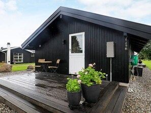 A black wooden building with a white door, two potted plants, and a small outdoor seating area with chairs. - 5 Person Holiday Home in Otterup (Otterup)