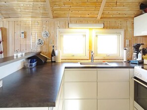 Une cuisine avec des murs en bois, un évier, une cuisinière et une fenêtre avec des stores.