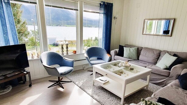 A living room with a TV, two blue chairs, a white coffee table, and a sofa with patterned cushions.