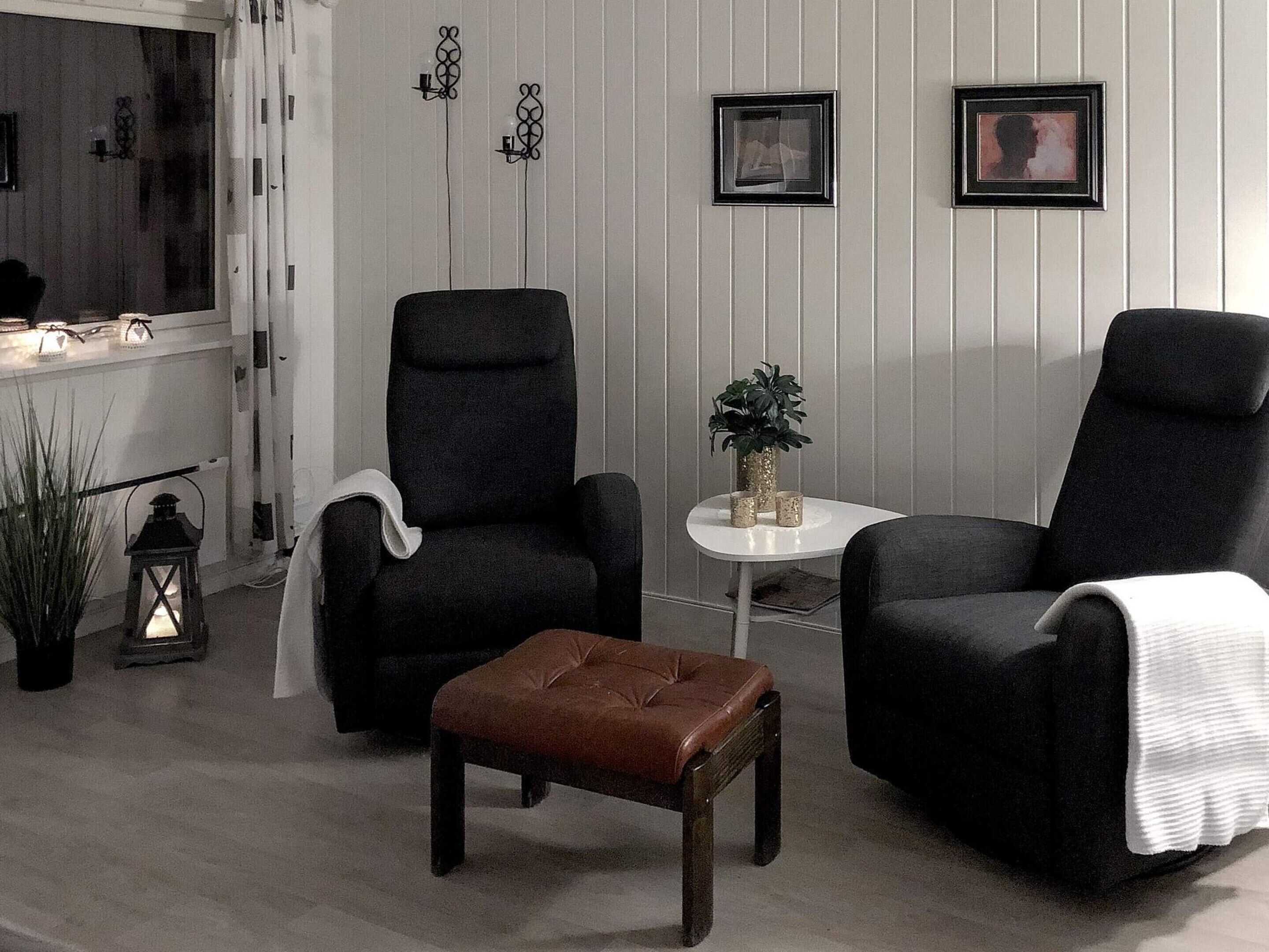 A room with two black armchairs, a small wooden table with a plant, and a brown ottoman.