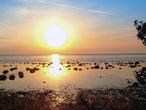 Pôr do sol sobre uma praia rochosa com águas calmas refletindo o sol.