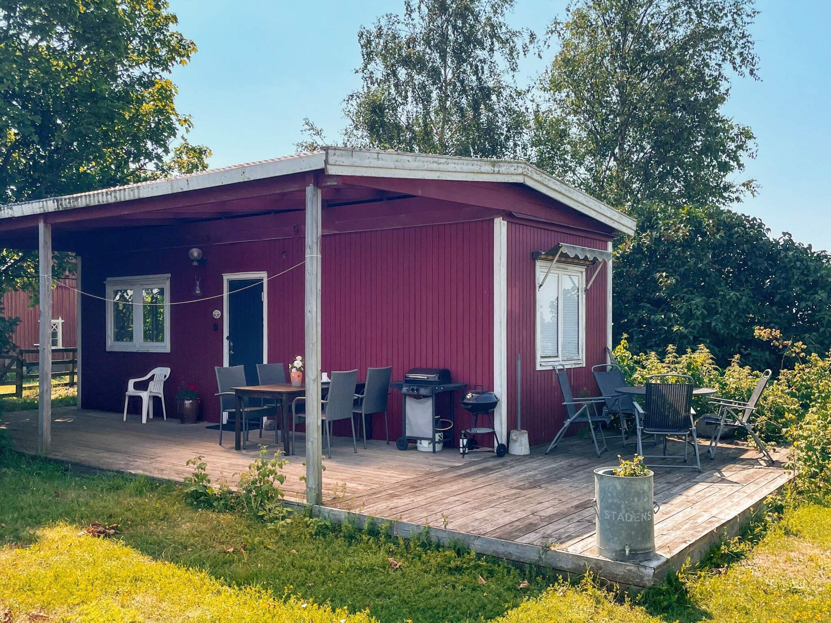 En röd träbyggnad med en täckt uteplats, utomhusmöbler och ett område med grill.