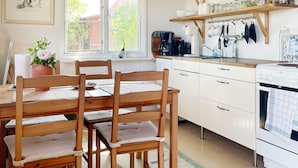A kitchen with wooden chairs, a dining table, white cabinets, and a window with a view of greenery. - 4 Person Holiday Home in Gotlands.tofta (Gotlands Tofta)