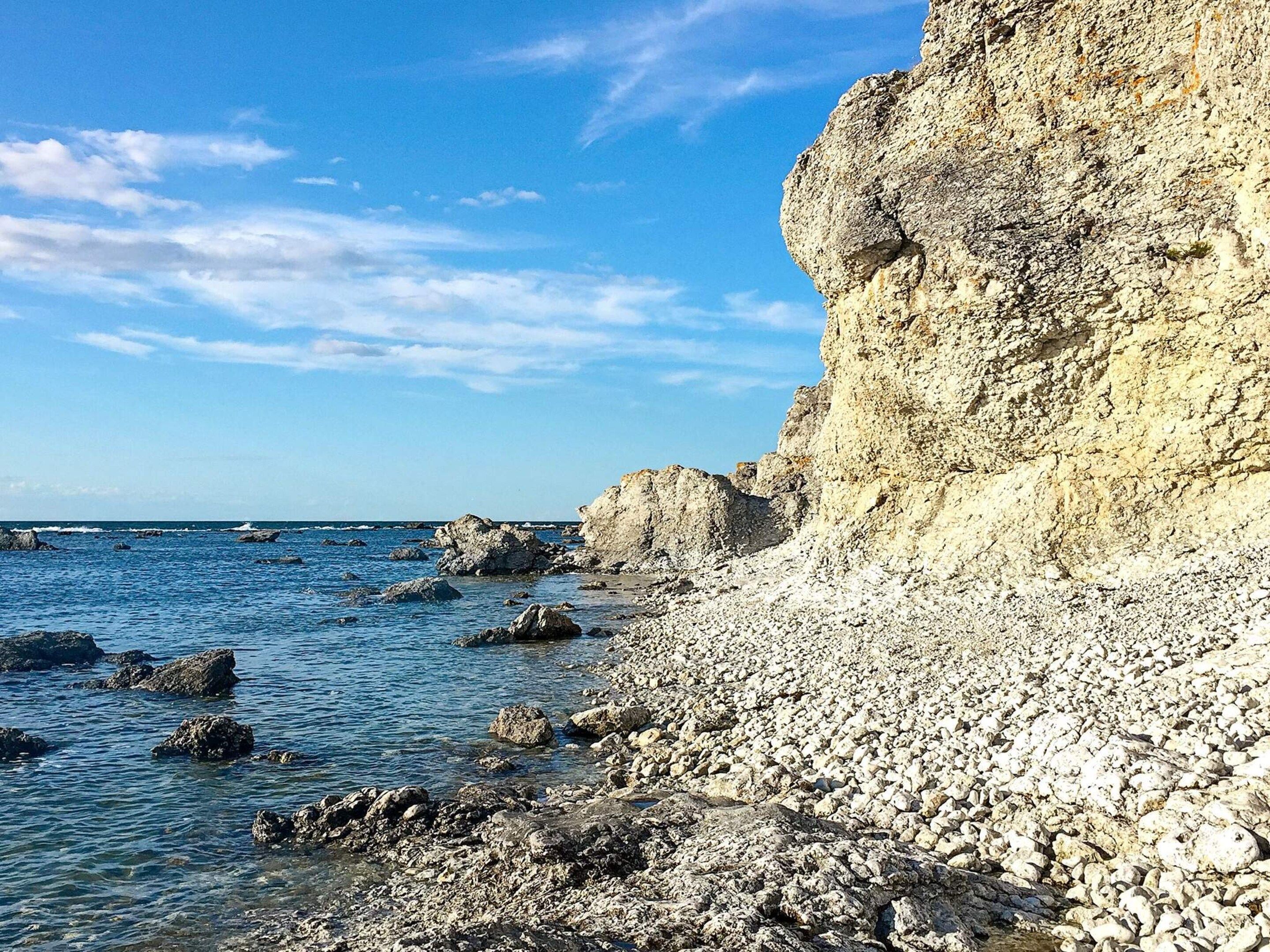 A rocky shoreline with clear blue water and a steep cliff.