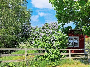 A red building with a window, surrounded by lush greenery and a wooden fence.