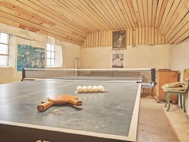 Una mesa de ping pong con pelotas y paletas, un techo de madera y un cartel en la pared.