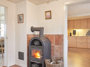 A room with a wood-burning stove, a wicker basket, and a kitchen area with cabinets.