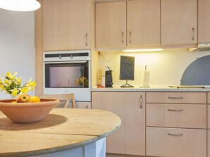 A kitchen with wooden cabinets, a round wooden table, a vase with flowers, and a blackboard with a welcome message.
