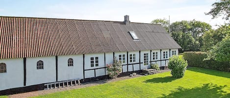 A traditional half-timbered house with a sloped roof, a small garden, and a clear sky.