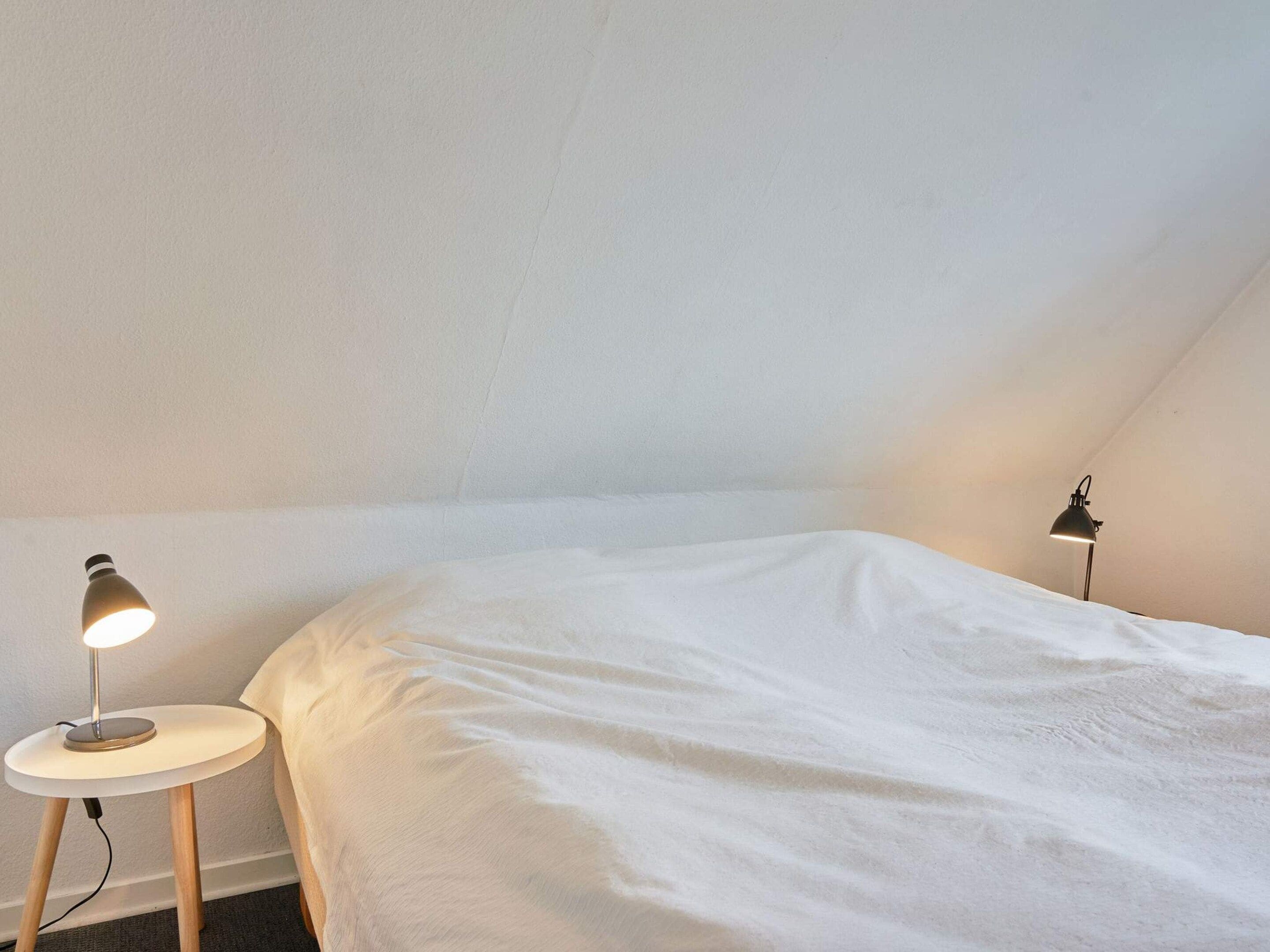 A bedroom with a single bed, two bedside lamps, and a small table.