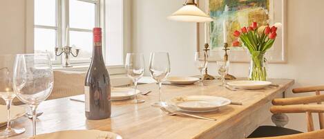 A dining table set with plates, glasses, and a bottle, with a vase of tulips and a painting on the wall.