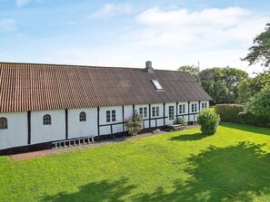 A traditional half-timbered house with a sloped roof, a small garden, and a clear sky.