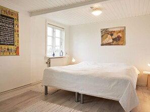 A bedroom with a bed, a window, a radiator, a painting, and a poster on the wall.