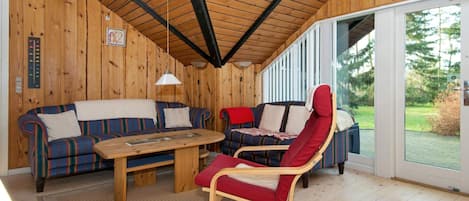 A wooden interior with a high ceiling, a sofa, a chair, and a table.