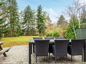 An outdoor patio with a table and chairs, surrounded by trees and a wooden fence. - 6 Person Holiday Home in Farvang (Farvang)