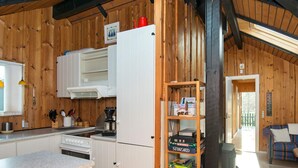 A wooden interior with a kitchen area, including a stove, refrigerator, and a shelf with board games. - 6 Person Holiday Home in Farvang (Farvang)
