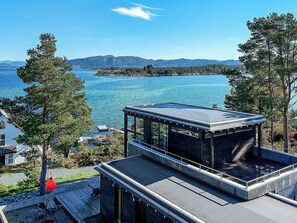 A modern building with a glass facade overlooking a body of water and a distant mountain range. - 6 Person Holiday Home in Mosterhamn (Bomlo)