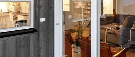 A room with a wooden wall, a window, a door, a sofa, a chair, and a table.